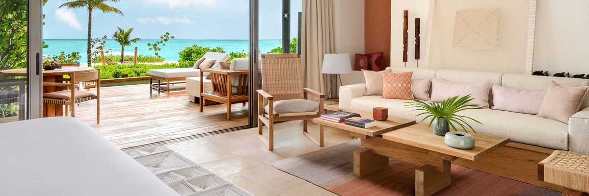 a hotel suite in neutral tones with a back deck that opens onto a beach and the ocean in the distance