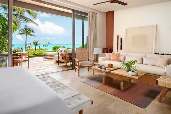 a hotel suite in neutral tones with a back deck that opens onto a beach and the ocean in the distance