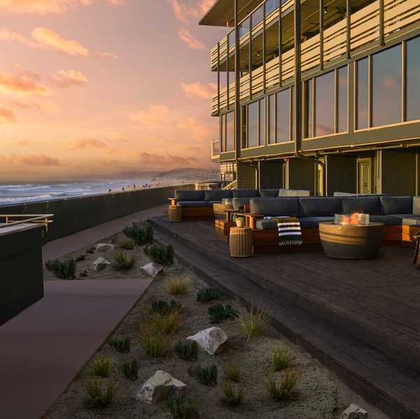 a hotel with a broad patio and seating on the beach in the sunset