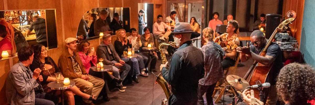 a jazz band playing in a small venue with wood-paneled walls and people sitting around the edges