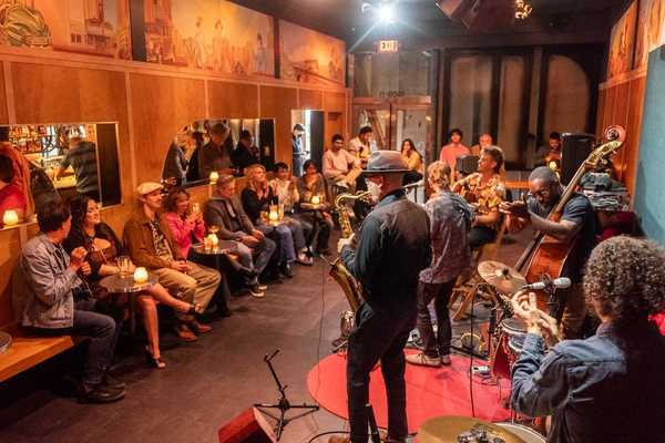 a jazz band playing in a small venue with wood-paneled walls and people sitting around the edges