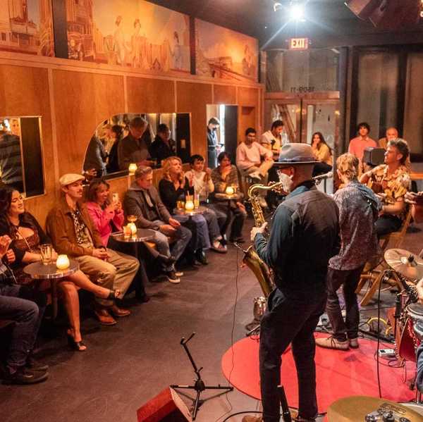 a jazz band playing in a small venue with wood-paneled walls and people sitting around the edges