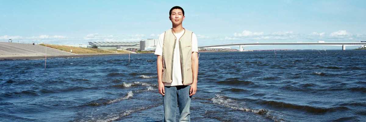 a Korean man standing in shallow water in front of a cityscape