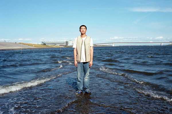 a Korean man standing in shallow water in front of a cityscape