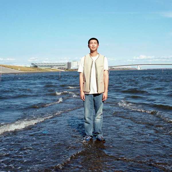 a Korean man standing in shallow water in front of a cityscape