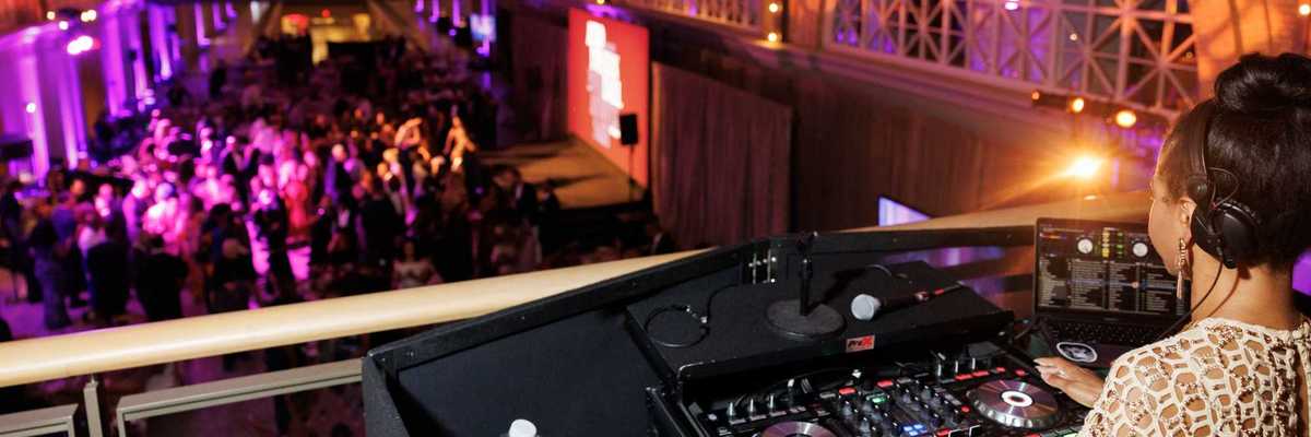 a large hall with purple lights, a dj, and people dancing