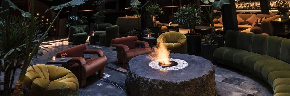 a living room like lounge with a fire pit and a bar in the background