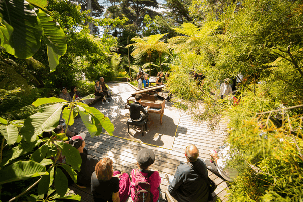 a man playing a grand piano on a stage in the middle of a garden