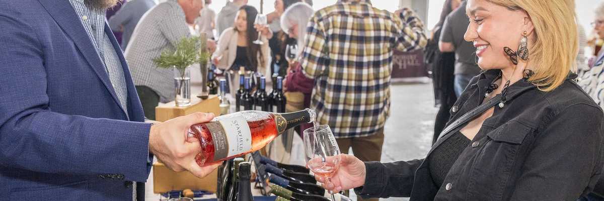 a man pouring wine into a glass for a woman at a wine festival