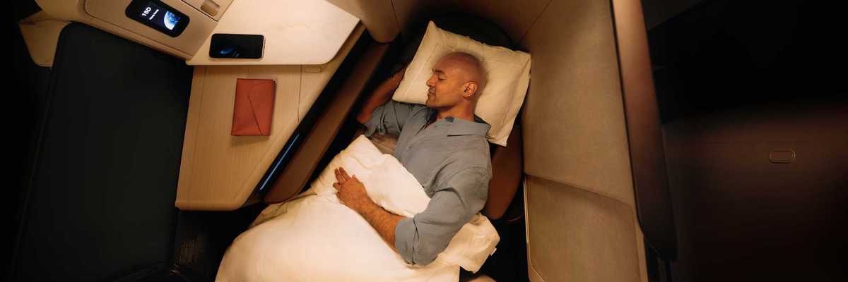 a man sleeping in an Aria Suite business class seat on a Cathay Pacific flight