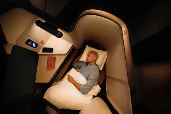 a man sleeping in an Aria Suite business class seat on a Cathay Pacific flight