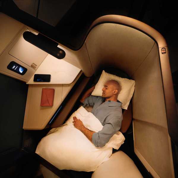 a man sleeping in an Aria Suite business class seat on a Cathay Pacific flight