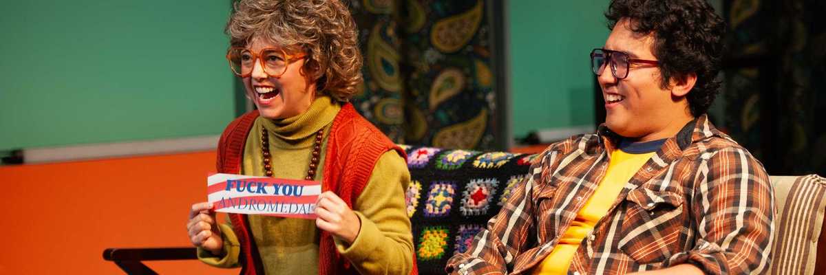 a middle aged woman and man in 1970s clothing laughing at a TV