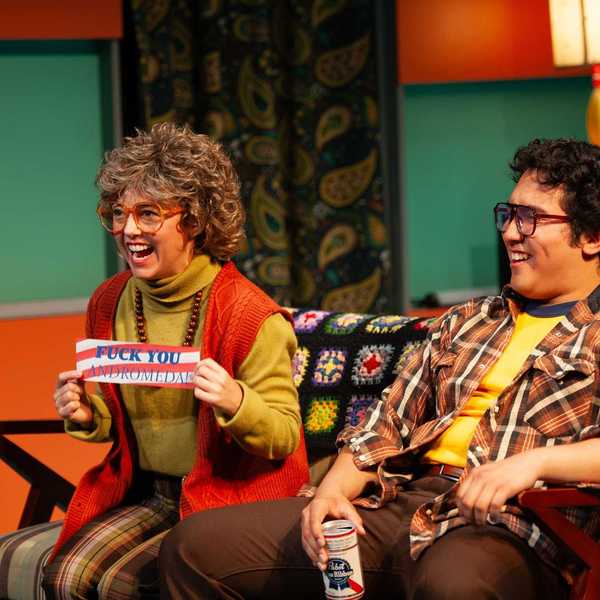 a middle aged woman and man in 1970s clothing laughing at a TV