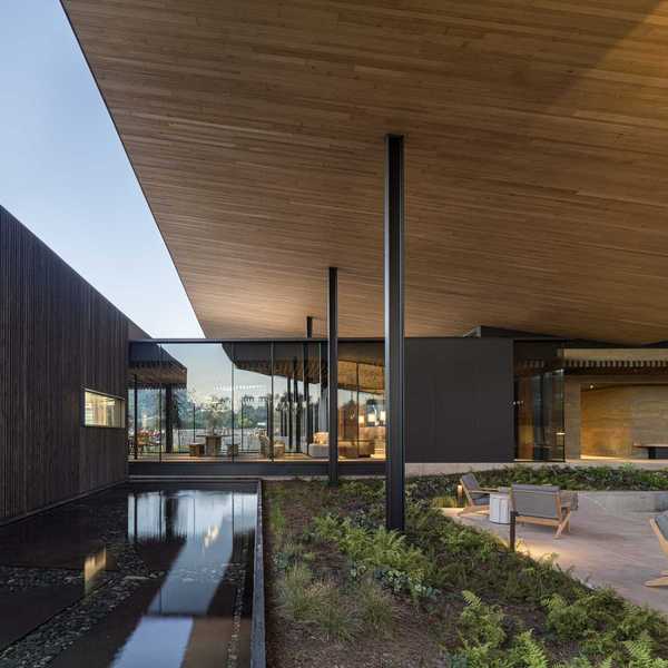 a modern architectural image with a shallow pool and a patio set with chairs
