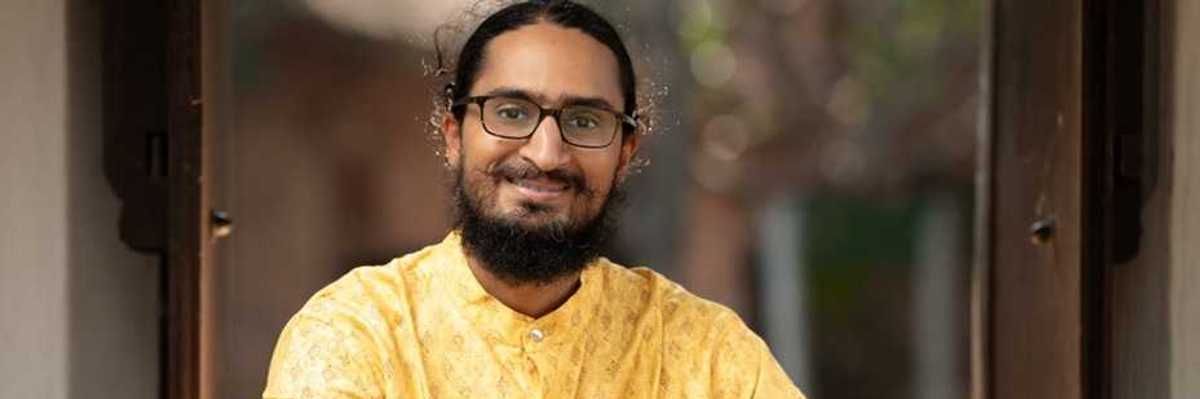 a musician in a yellow Indian-style shirt holding a double-sided drum