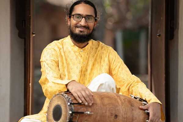 a musician in a yellow Indian-style shirt holding a double-sided drum