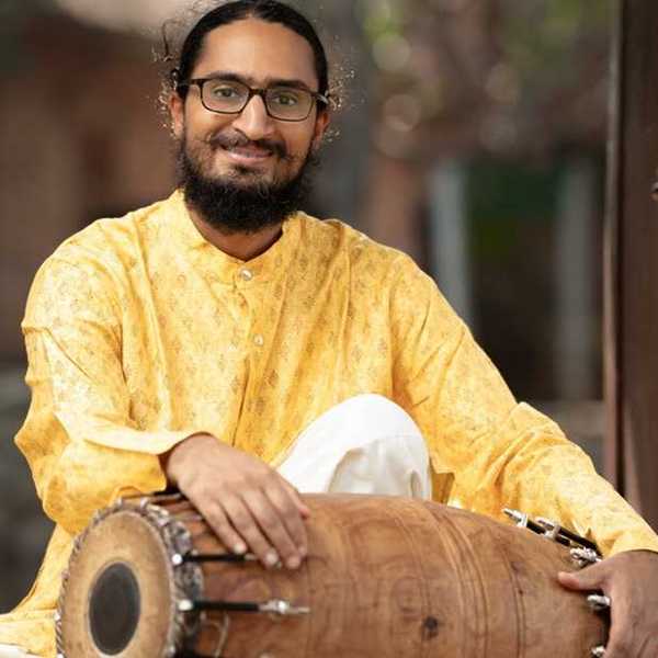 a musician in a yellow Indian-style shirt holding a double-sided drum