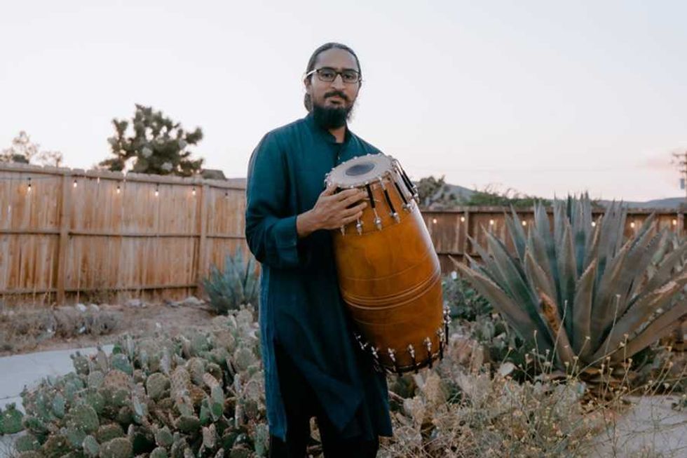 a musician with a two-sided Indian drum standing in a garden of succulents