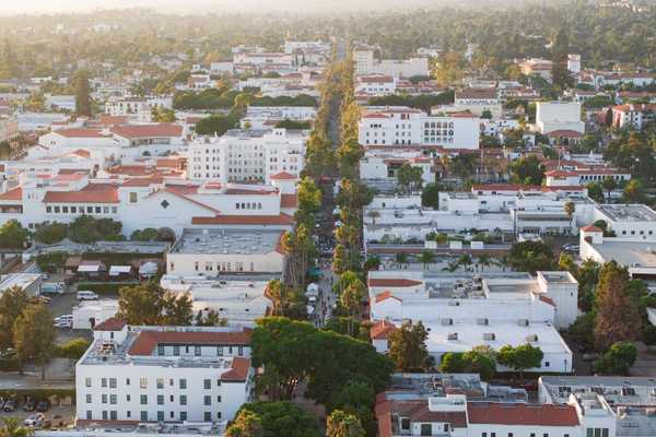 a neighborhood of white-washed buildings with red tiled roofs around a main street lined with trees