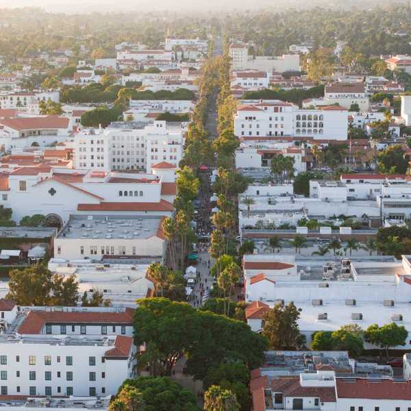 a neighborhood of white-washed buildings with red tiled roofs around a main street lined with trees