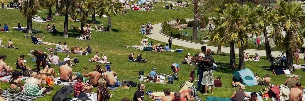 a park filled with people sitting on blankets with the SF city skyline behind