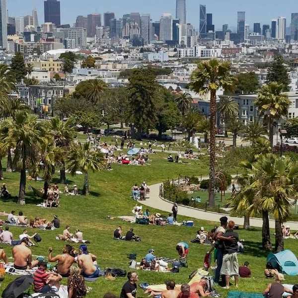 a park filled with people sitting on blankets with the SF city skyline behind