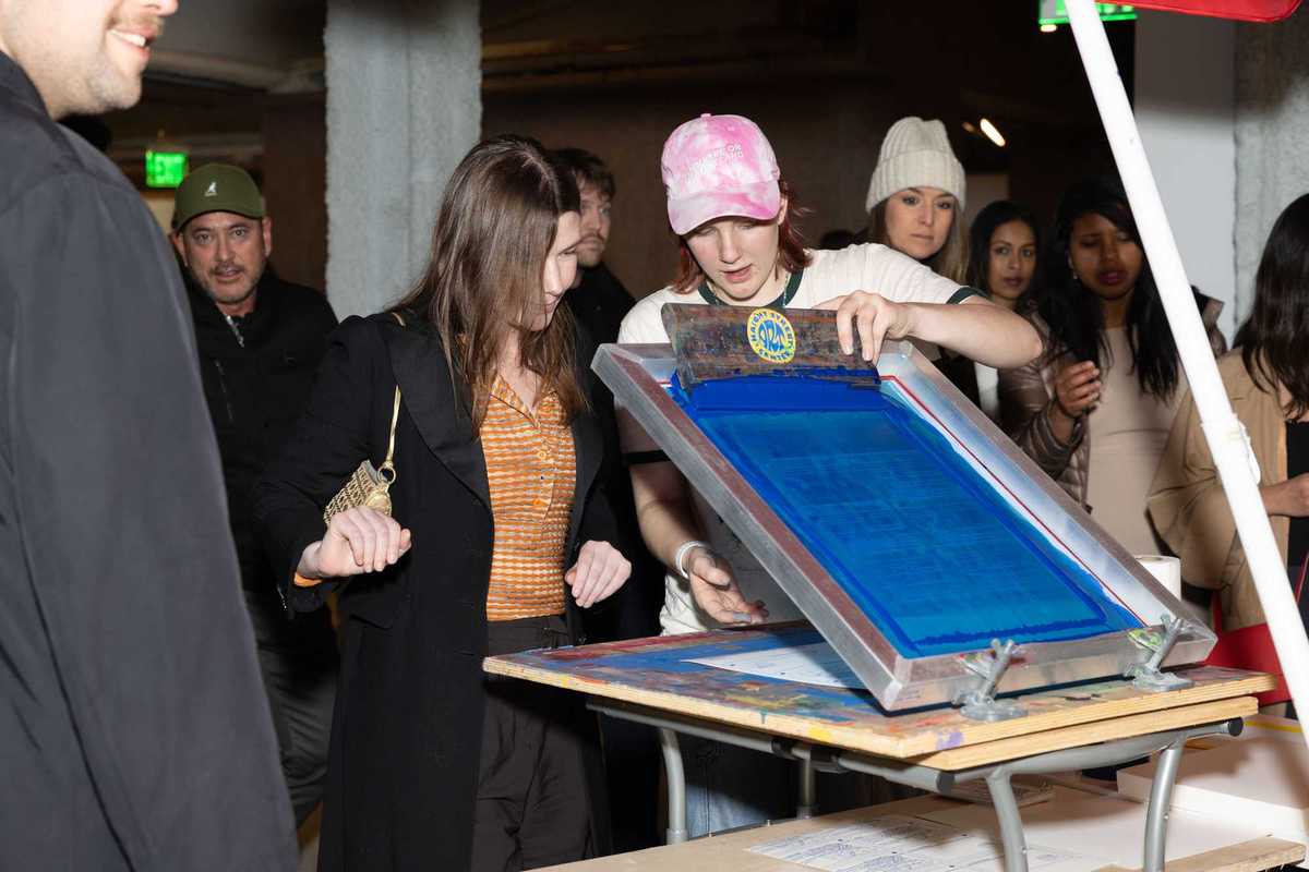 a person hand screen printing a poster with other people watching
