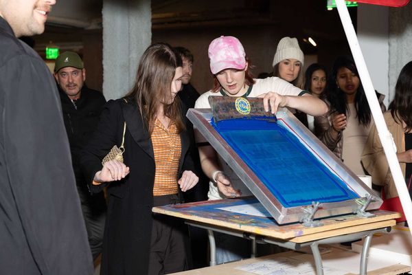 a person hand screen printing a poster with other people watching