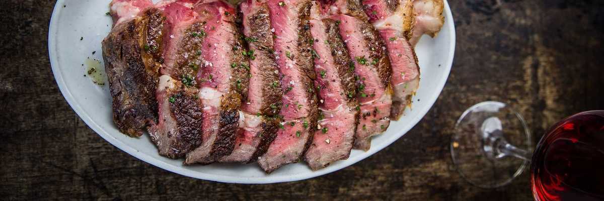 a plate of cut ribeye with a bottle and glass of red wine on the table