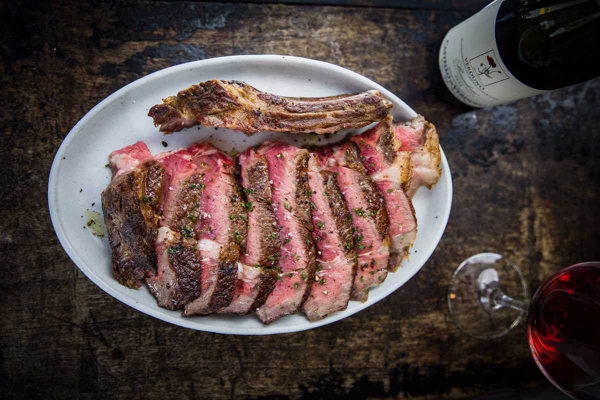 a plate of cut ribeye with a bottle and glass of red wine on the table