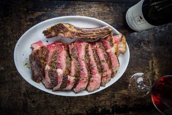 a plate of cut ribeye with a bottle and glass of red wine on the table