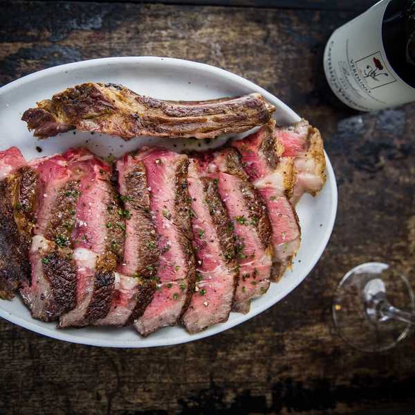 a plate of cut ribeye with a bottle and glass of red wine on the table