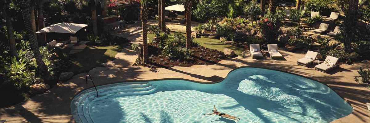 a pool with a person floating in it surrounded by palm trees and desert mountains