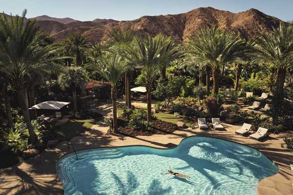 a pool with a person floating in it surrounded by palm trees and desert mountains