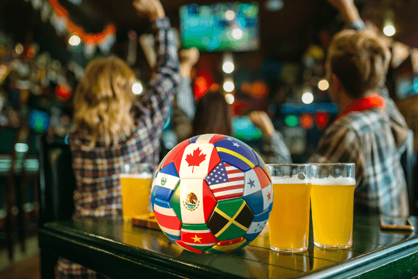 a soccer bar and pints of beer on a table with cheering fans in a bar behind