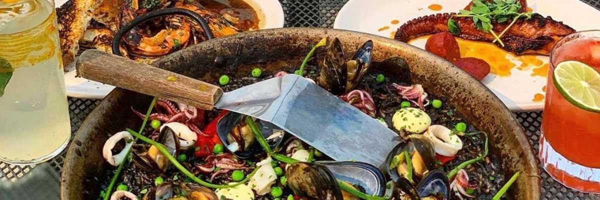 a table of Spanish food including a black paella