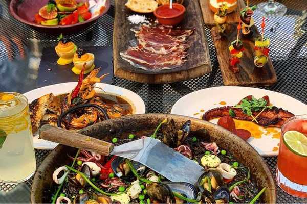a table of Spanish food including a black paella