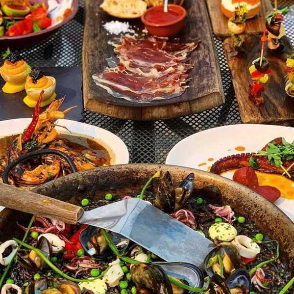 a table of Spanish food including a black paella