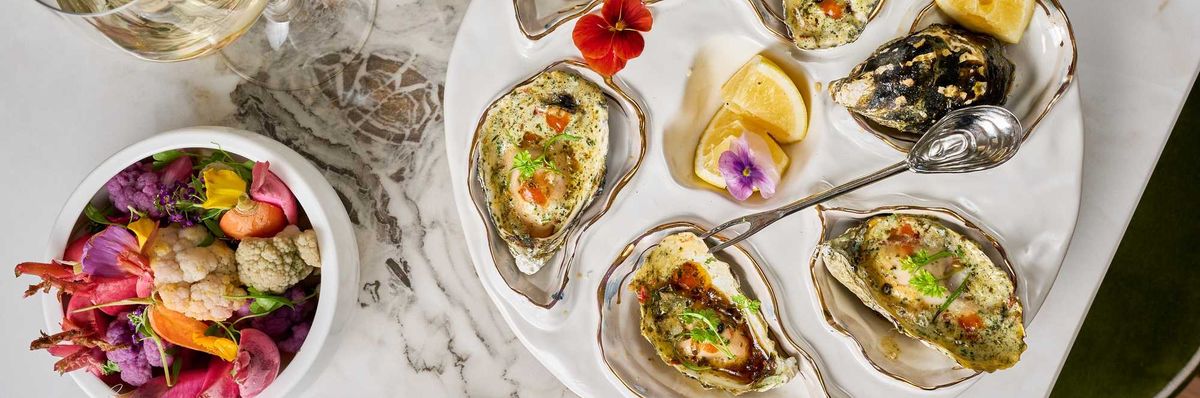 A table spread with beautiful grilled oysters and pickled veggies and wine