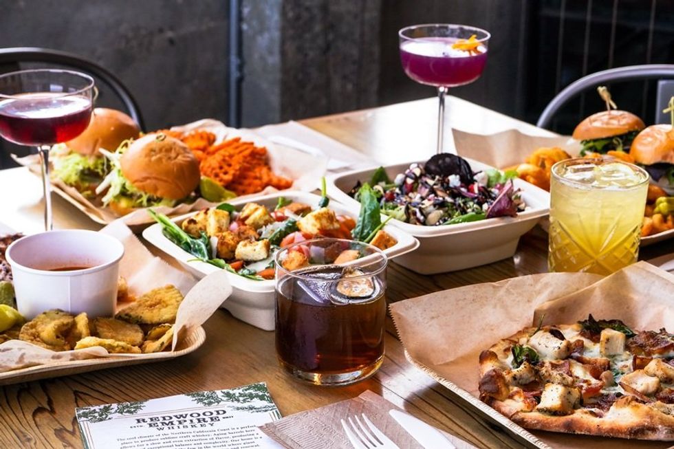 A variety of dishes and drinks on a table, including pizza, burgers, salad, and cocktails.