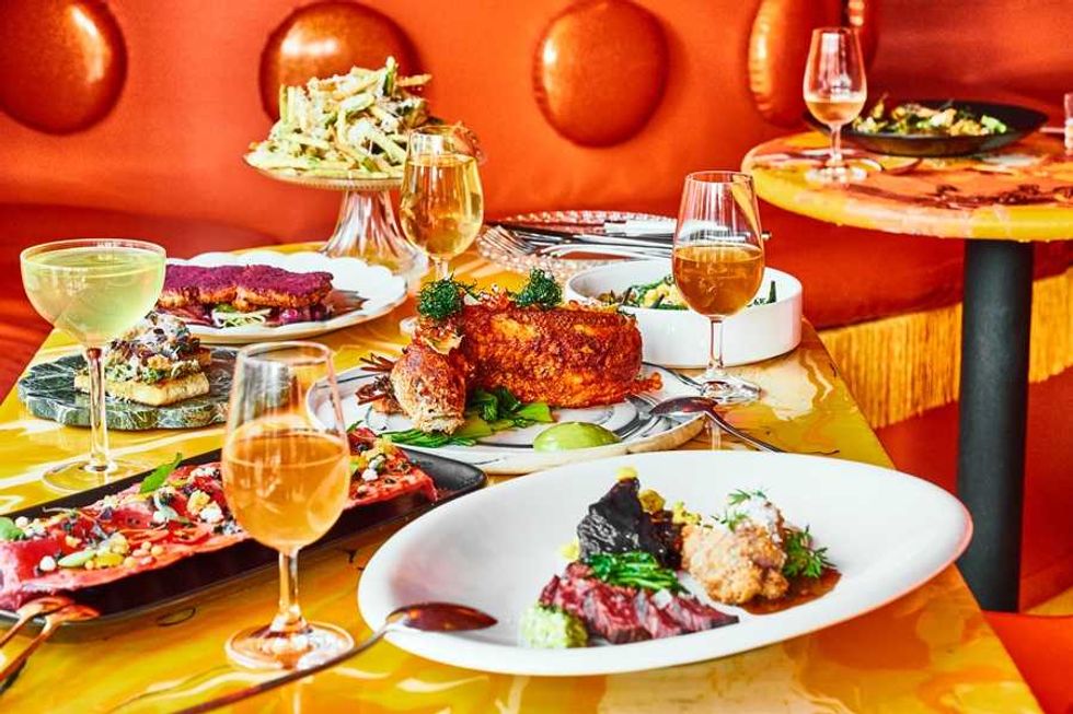 A vibrant table setting with gourmet dishes and cocktails on an orange-themed background.
