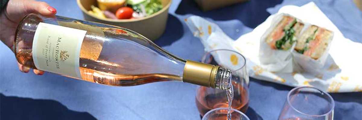 a wine bottle pouring rose in glasses on a blue picnic blanket with food