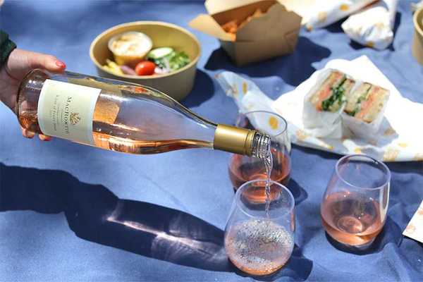 a wine bottle pouring rose in glasses on a blue picnic blanket with food