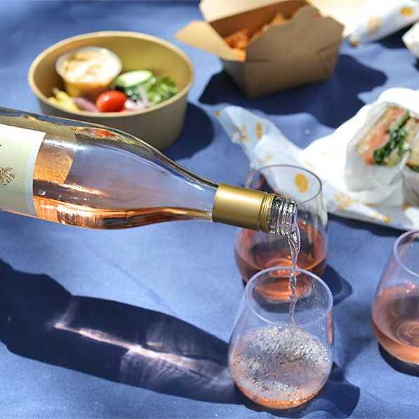 a wine bottle pouring rose in glasses on a blue picnic blanket with food
