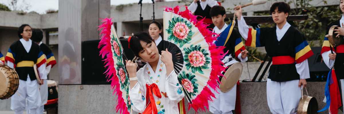 a woman doing a fan dance in traditional clothing with drummers behind her