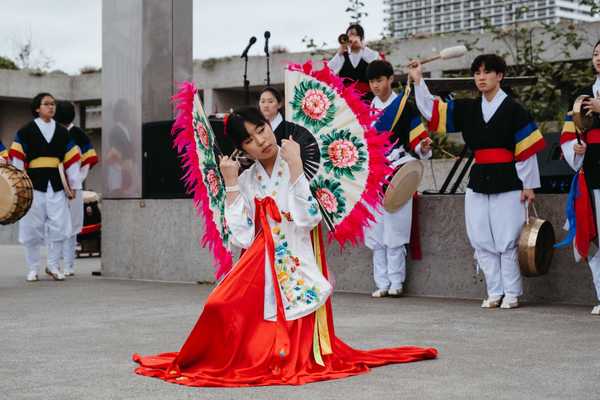 a woman doing a fan dance in traditional clothing with drummers behind her