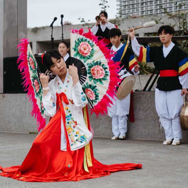 a woman doing a fan dance in traditional clothing with drummers behind her
