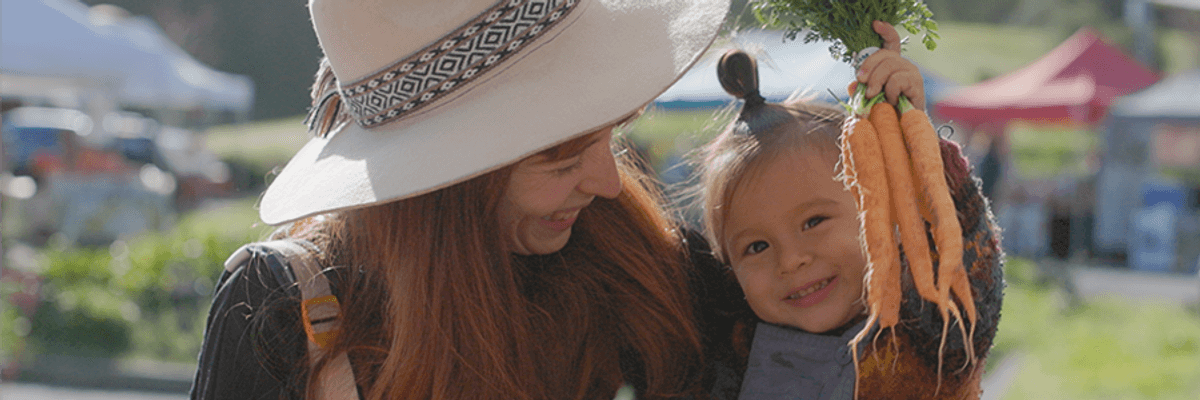 a woman holding a toddler who is holding a bunch of carrots