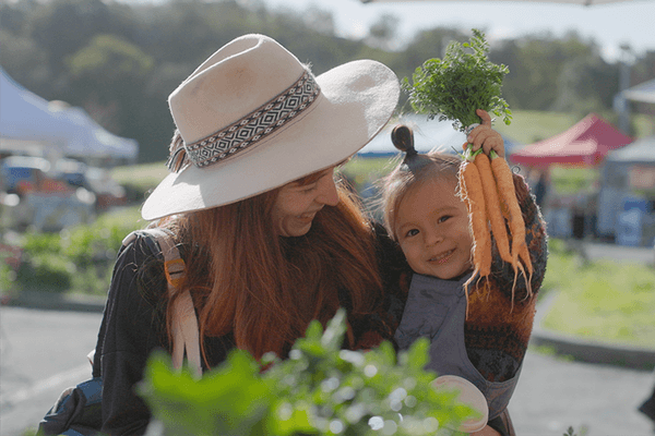 a woman holding a toddler who is holding a bunch of carrots